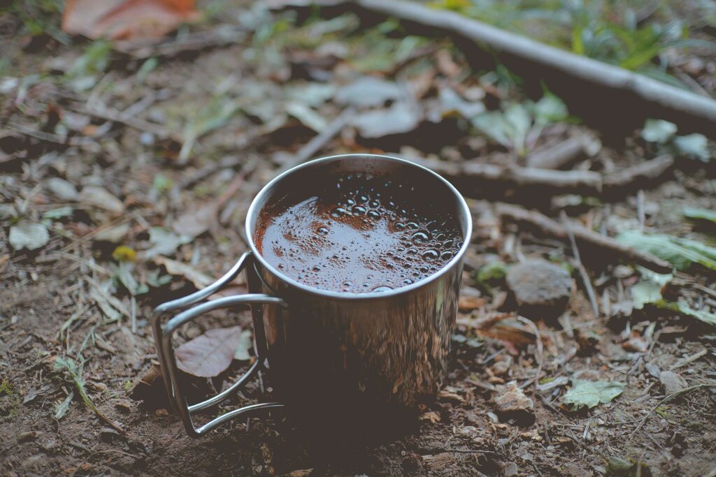 Rustic Metal Mug with Coffee Amidst Forest Foliage Wallpaper