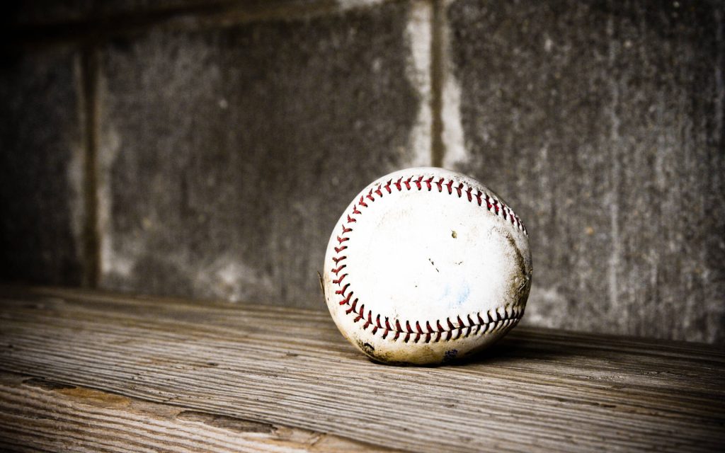 Weathered baseball with red stitching on wooden surface against gritty concrete background wallpaper