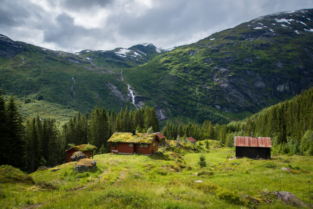 Rustic houses among lush grass and trees with mountains and waterfall scenic wallpaper background