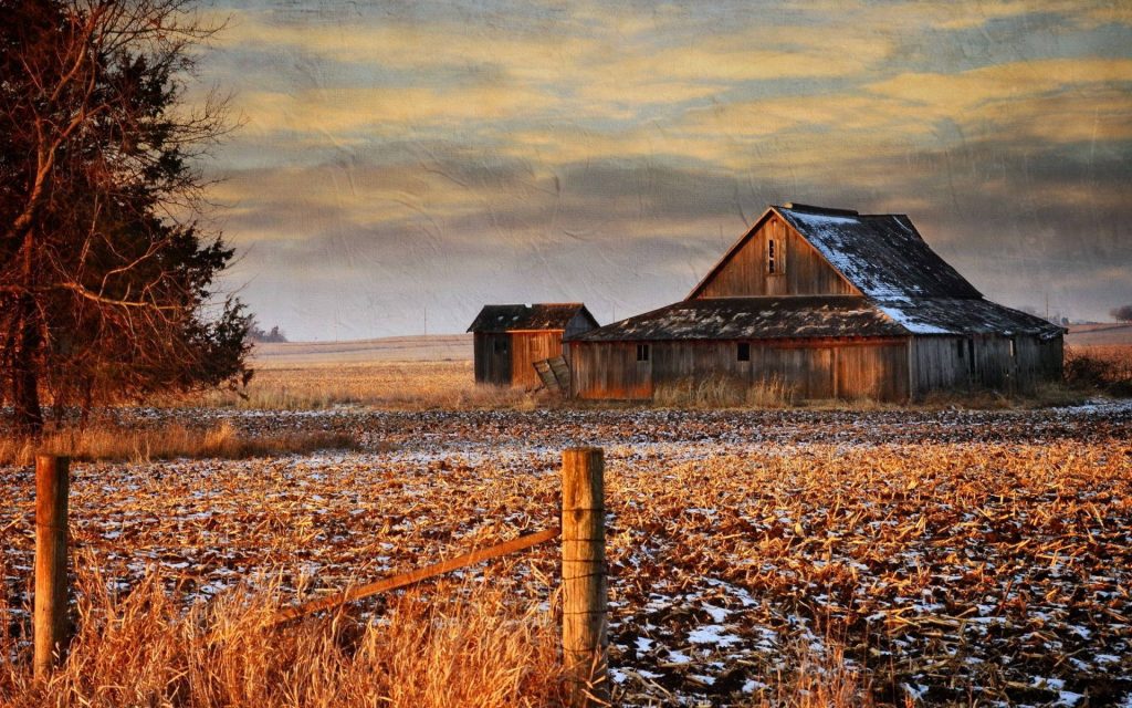 Weathered old barn in snowy harvested field with rustic fences under golden cloudy sky fall wallpaper