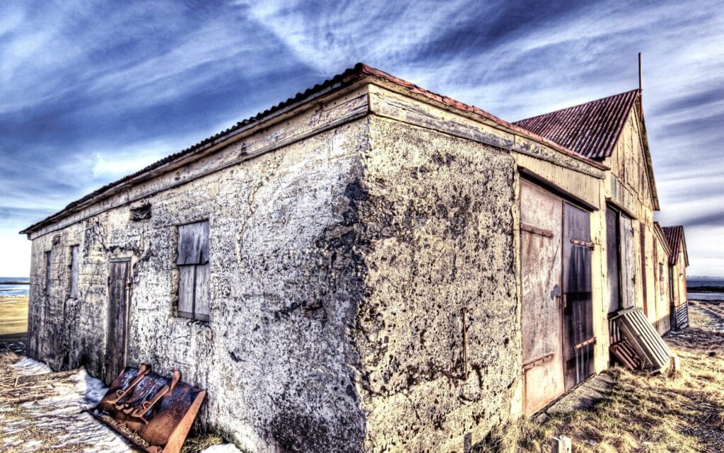 Rustic old stone house with weathered wood doors under moody sky in rural landscape wallpaper