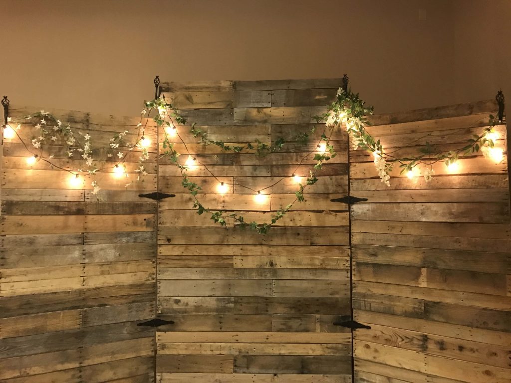 Rustic pallet wall backdrop with warm string lights and ivy vines for high school celebration Wallpaper