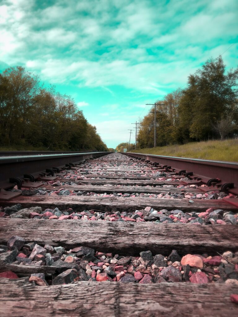 Rustic railway tracks through green trees under bright turquoise sky scenic wallpaper background