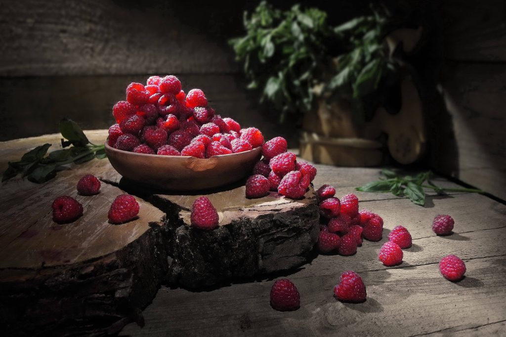 Rustic bowl of spilled raspberries on wooden logs with warm dramatic lighting wallpaper