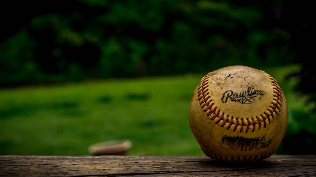 Scuffed Rawlings baseball on rustic wood with soft green outdoor background wallpaper