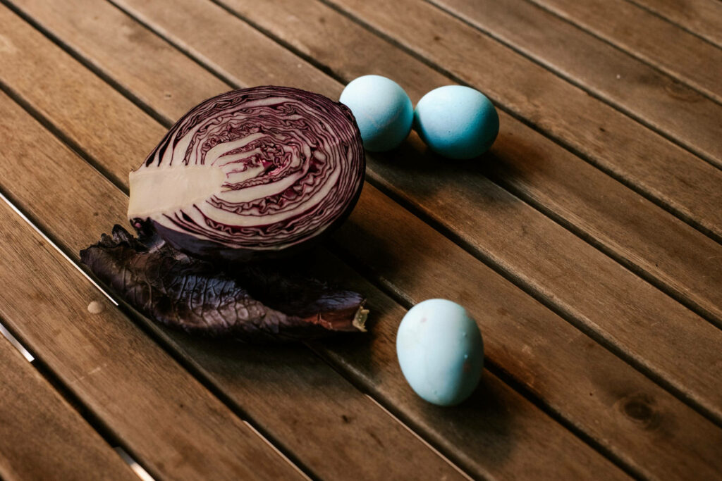Rustic wallpaper with halved red cabbage and pastel blue eggs on wooden tabletop background
