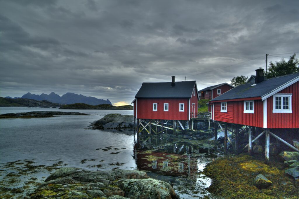 Red stilt houses on rocky coast with calm water and dramatic cloudy sky seaside wallpaper