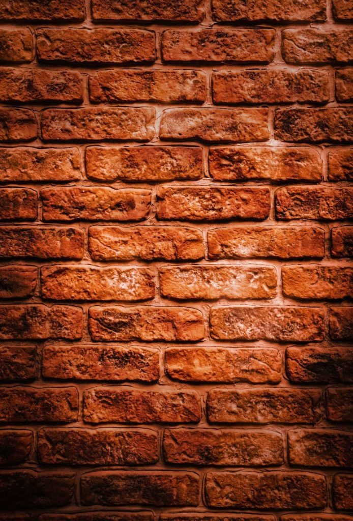 Rustic uneven textured brick wall background warm reddish brown tones dramatic vignette lighting Wallpaper