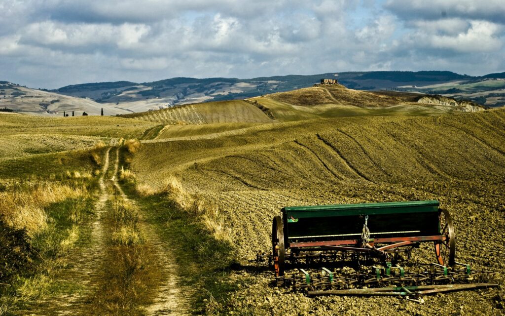 Rustic plow in earthy rural fields under partly cloudy sky with winding dirt road wallpaper background