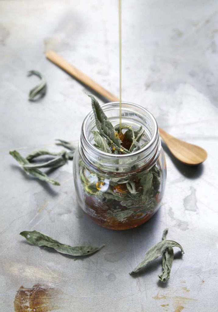 Rustic wallpaper of sage leaves in jar with honey drizzle wooden spoon on gray textured surface