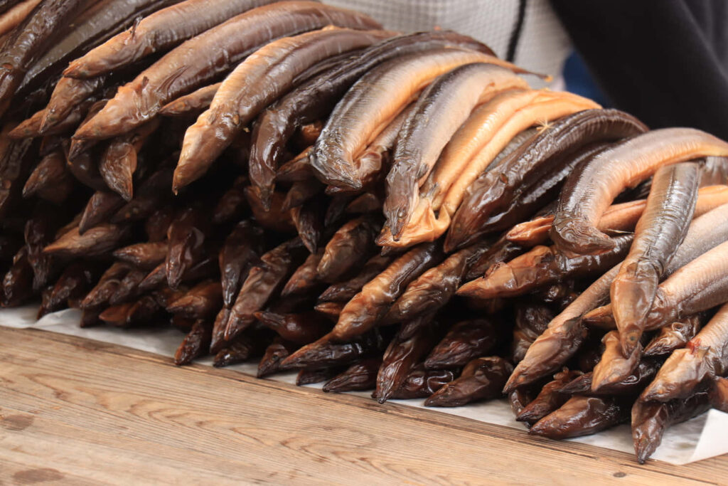 Close-up of stacked smoked eels with shiny brown-black skin on wooden surface rustic wallpaper