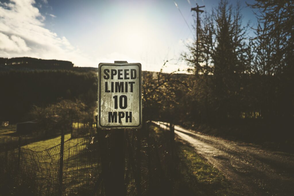 Rustic speed limit sign by quiet country road with sunlight filtering through trees and fields Wallpaper