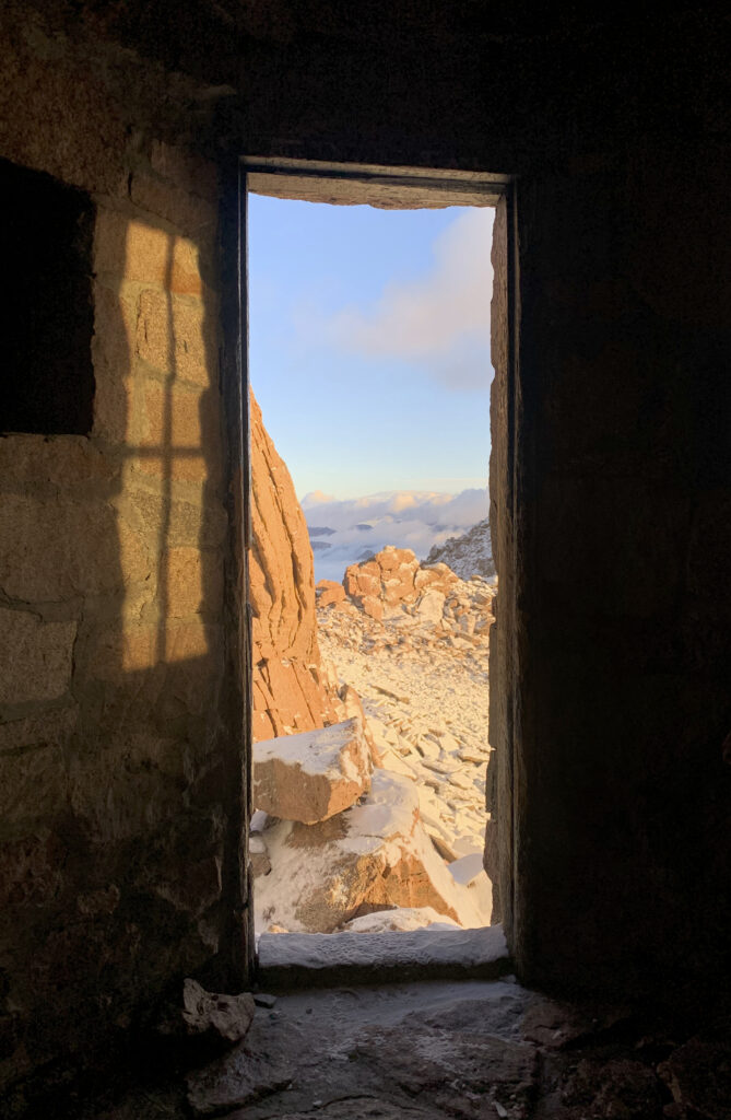 Rustic stone doorway framing sunlit rocks and rolling hills under a soft blue sky wallpaper background