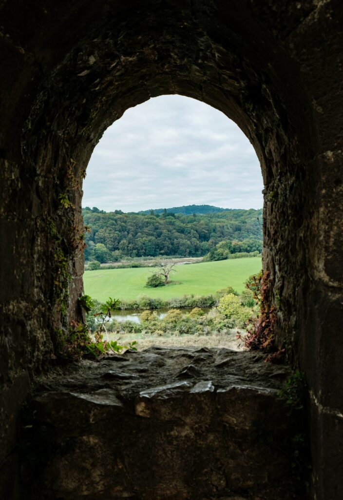 Rustic stone window framing rolling green hills forest and open sky scenic landscape wallpaper