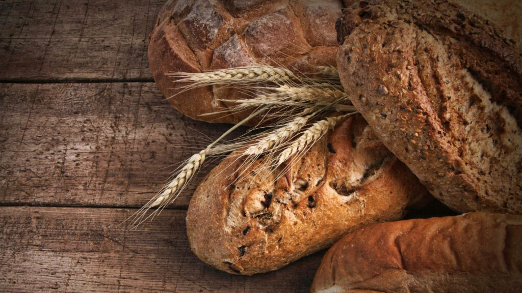 Rustic toasted artisan bread with raw wheat spikes on wooden textured background wallpaper