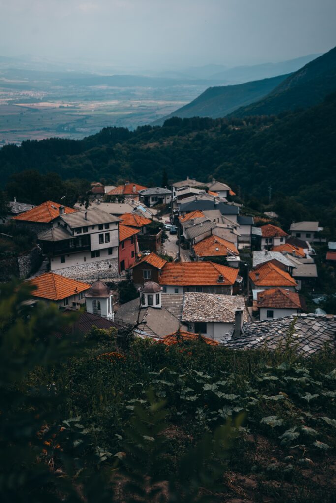 Quaint village with red-tiled roofs on rolling hills surrounded by forest and mountains wallpaper