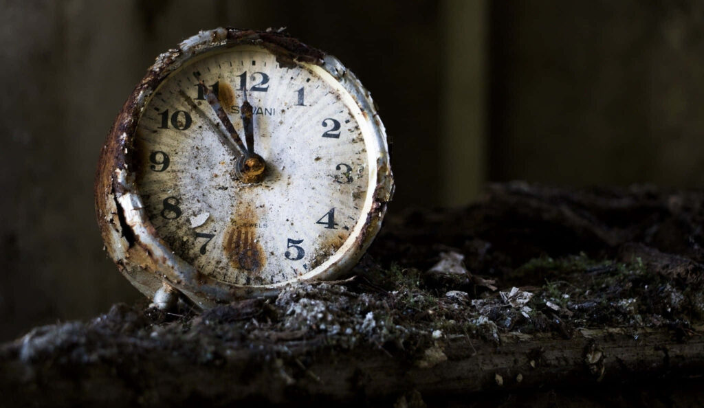 Old weathered clock with peeling paint on mossy wooden shelf symbolizing time passage wallpaper