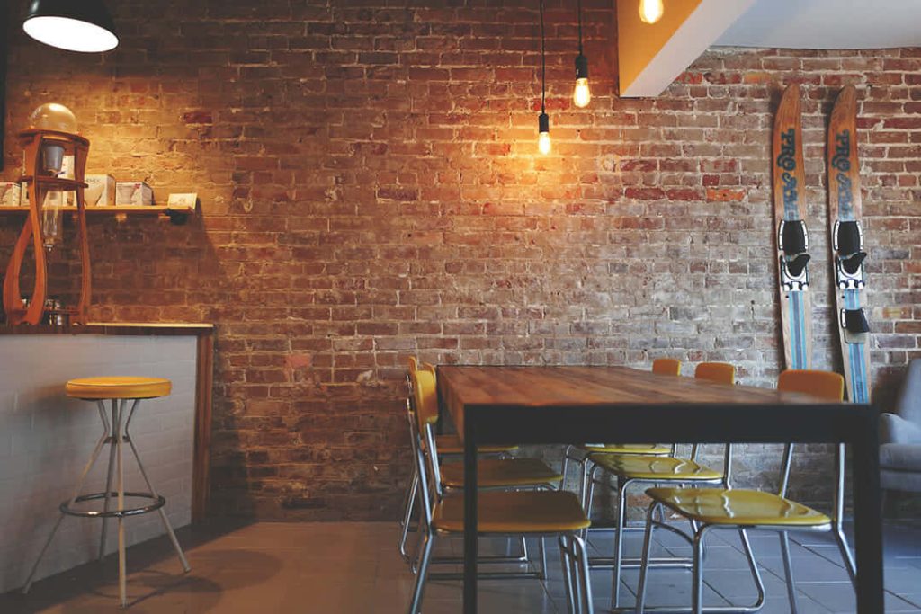 Rustic virtual Zoom background with cozy dining space exposed brick warm lighting yellow chairs Wallpaper