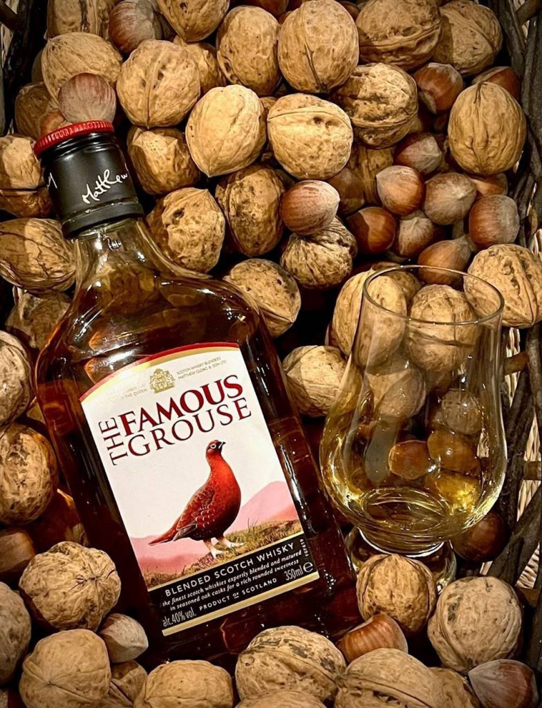 The Famous Grouse Scotch Whisky bottle and glass with walnuts and hazelnuts rustic background Wallpaper