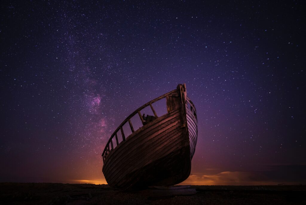 Weathered boat grounded under vibrant purple orange starry sky nightscape wallpaper background