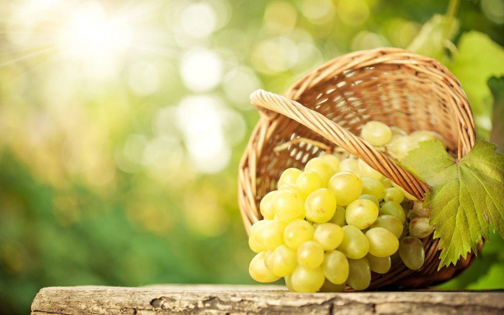 Rustic wicker basket with fresh green grapes on weathered wood in golden hour garden light Wallpaper