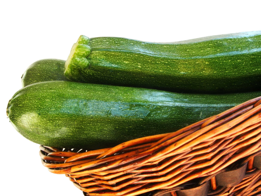 Close-up of rustic wicker basket with fresh green zucchinis on white background wallpaper