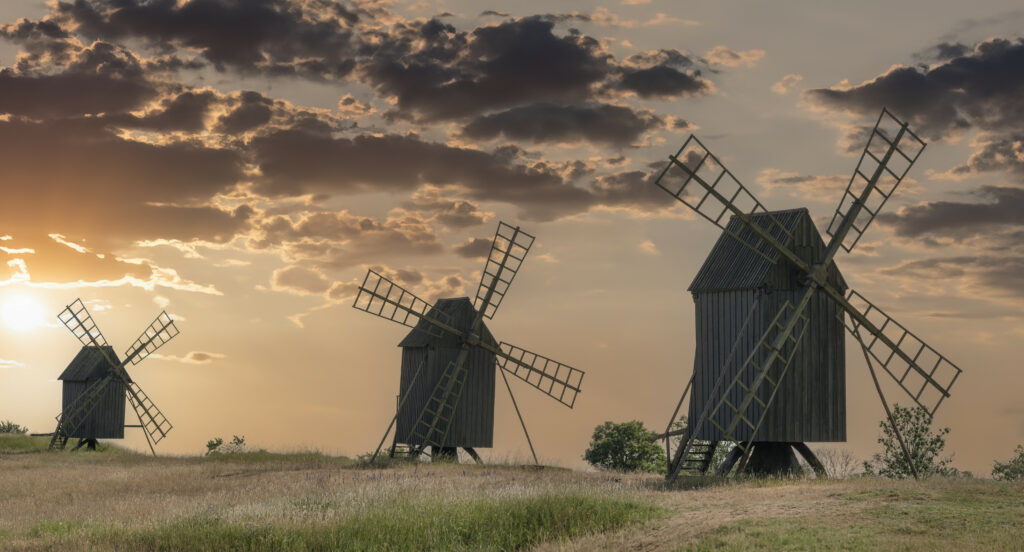 Three rustic windmills in grassy field at sunset with warm orange golden hues wallpaper background