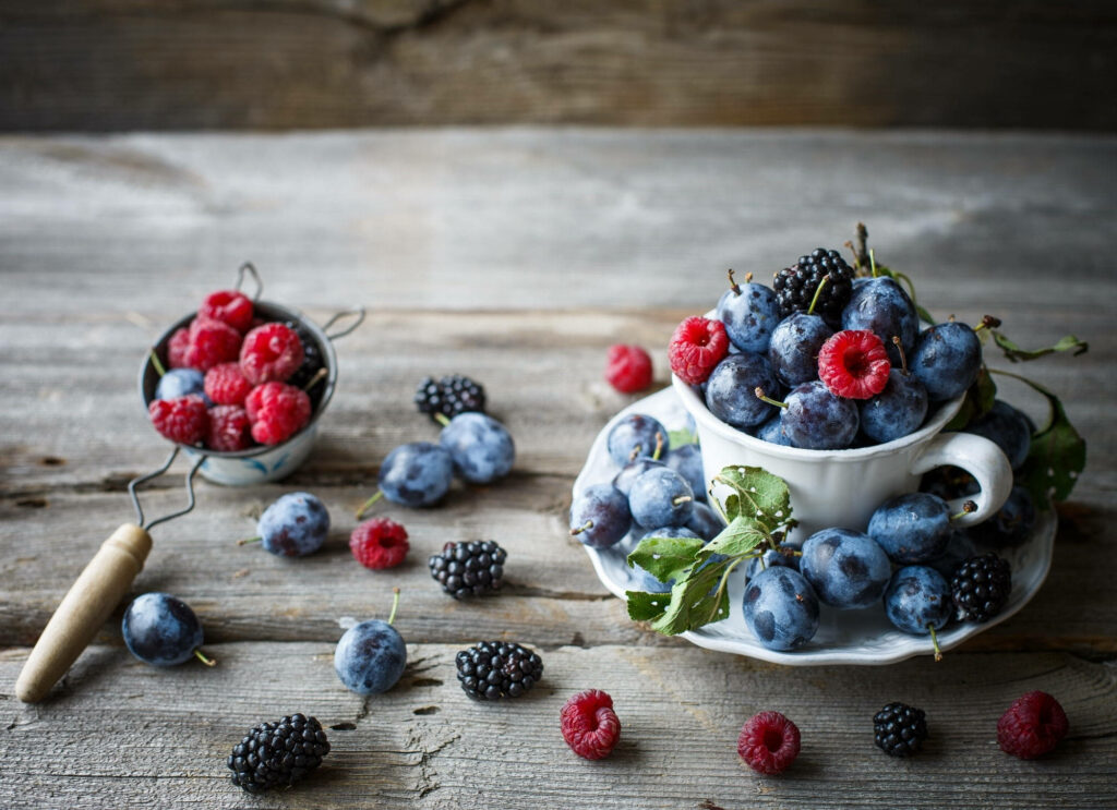 Rustic wooden background with fresh huckleberries raspberries and blackberries in teacup and strainer Wallpaper