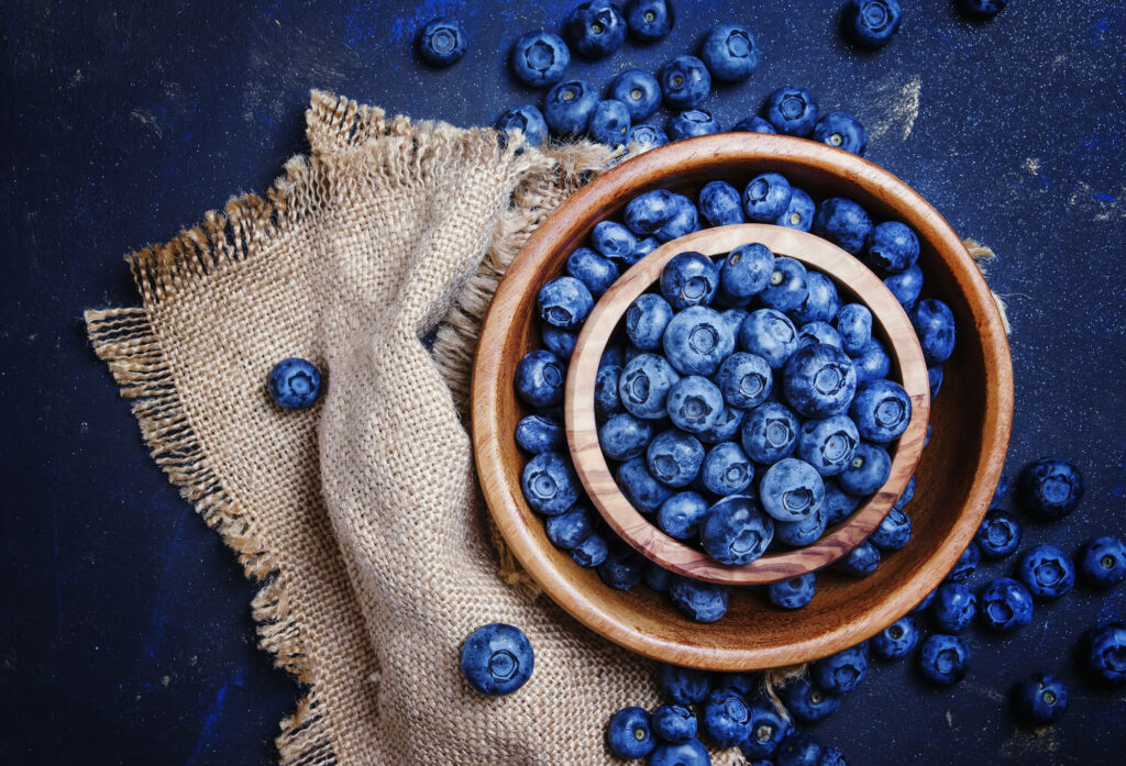 Rustic wooden bowl of fresh blueberries on textured burlap cloth vibrant natural flat lay wallpaper
