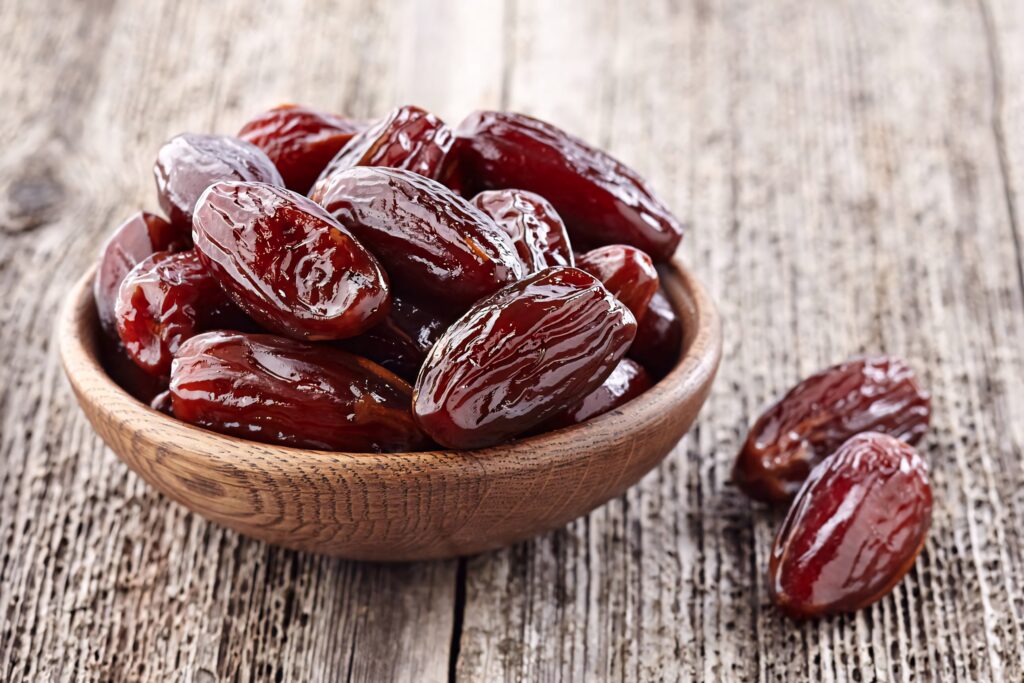 Rustic wooden bowl of glossy organic red dates on textured wood background high resolution wallpaper