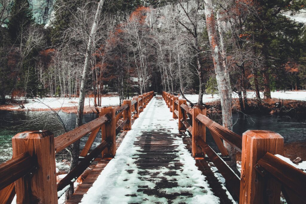 Rustic wooden bridge with melting snow and bare trees in early spring forest wallpaper background