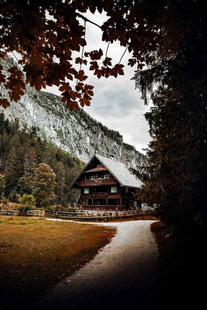 Rustic wooden cabin nestled among rocky mountains beside winding road with overhanging trees Wallpaper