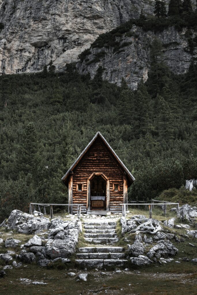 Rustic wooden house amid rocks and green landscape at mountain base peaceful nature scene Wallpaper