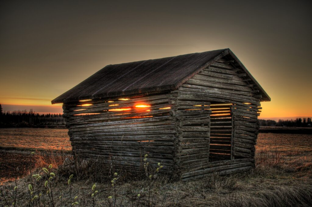 Rustic wooden house in open field at golden sunset peaceful rural landscape wallpaper background