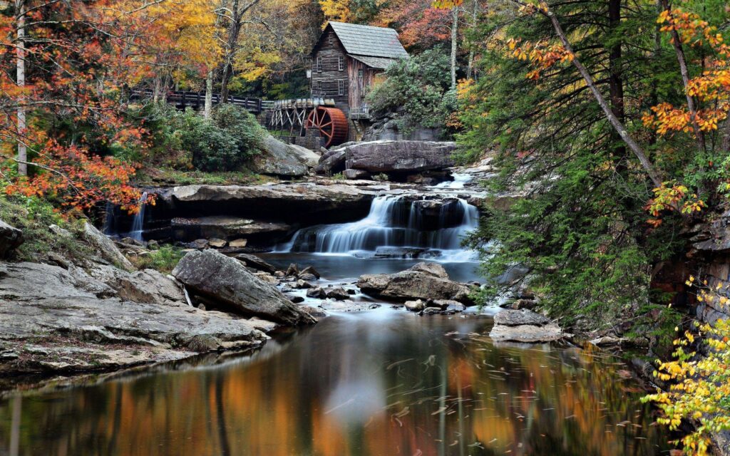 Rustic wooden mill by flowing river with autumn trees and cascading waterfall serene landscape Wallpaper