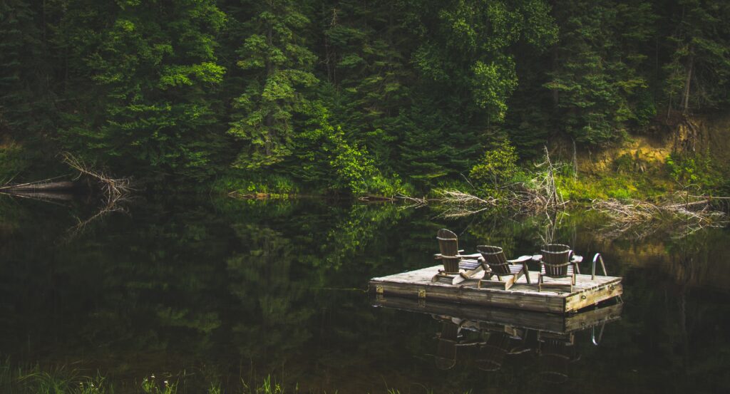 Rustic wooden raft with cozy chairs on calm river surrounded by lush forest nature retreat wallpaper