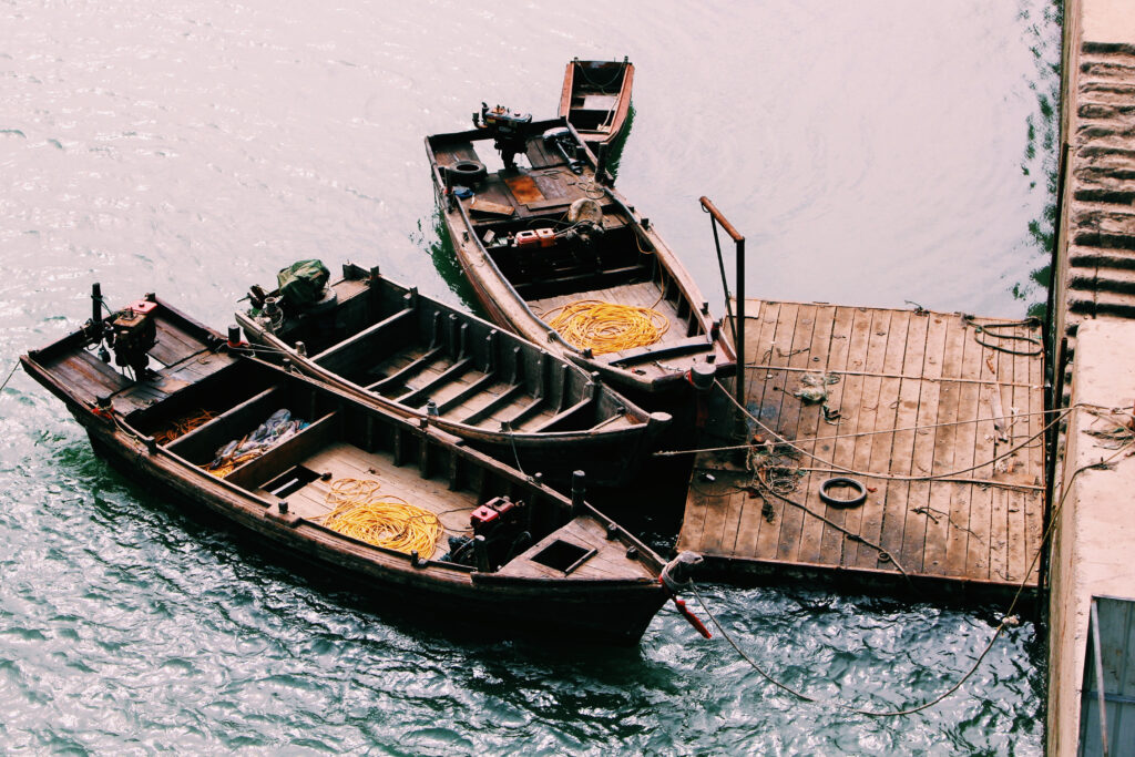 Rustic wooden ships moored at peaceful river pier with blue green water and coiled ropes wallpaper