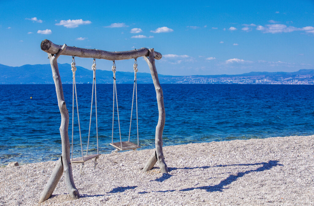 Rustic wooden beach swing overlooking calm blue sea and vibrant summer sky coastal retreat Wallpaper