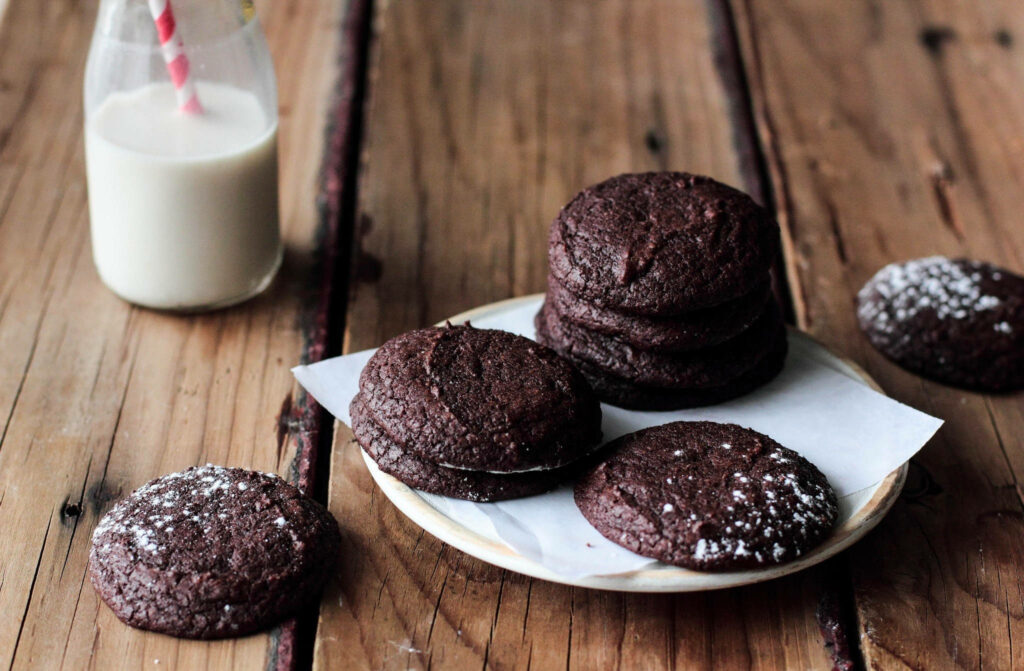 Rustic wooden table with chocolate cookies dusted with powdered sugar and milk bottle background Wallpaper