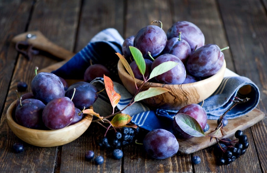 Rustic wooden table with fresh plums and blackberries in wooden bowls vibrant fruit background Wallpaper