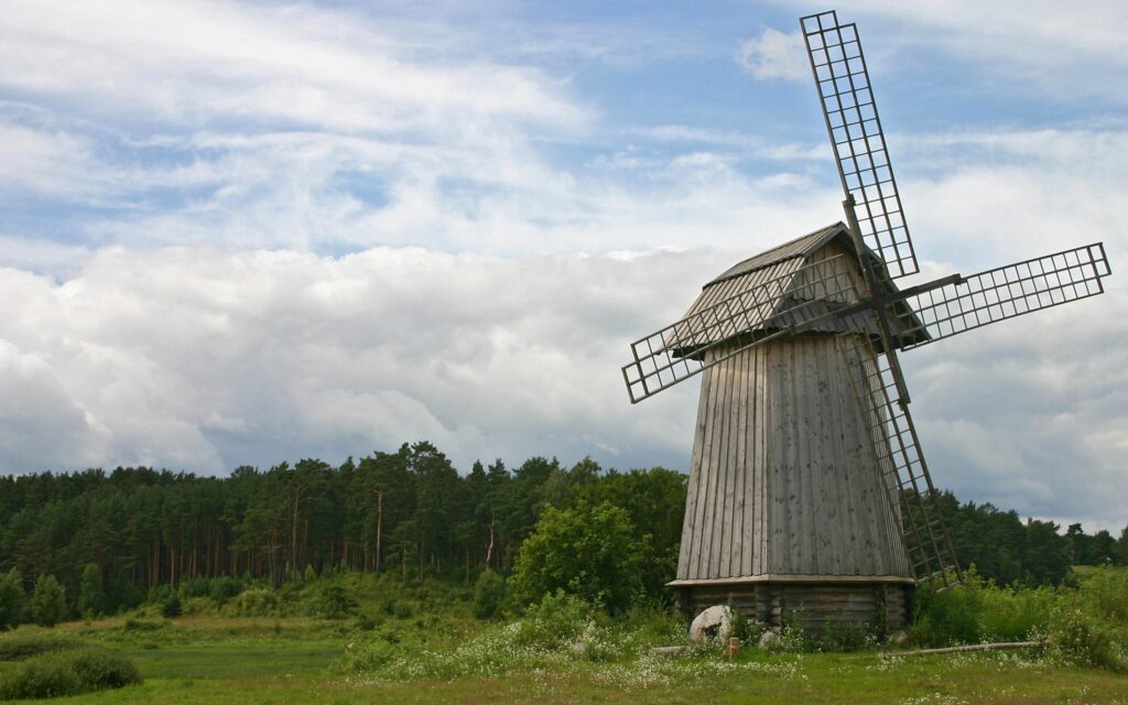 Rustic wooden windmill with lattice wings in green meadow under bright partly cloudy sky rural scene Wallpaper