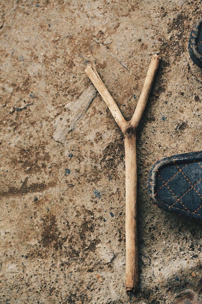 High-angle photo of Y-shaped dry stick on textured concrete near quilted dark shoe minimalist wallpaper