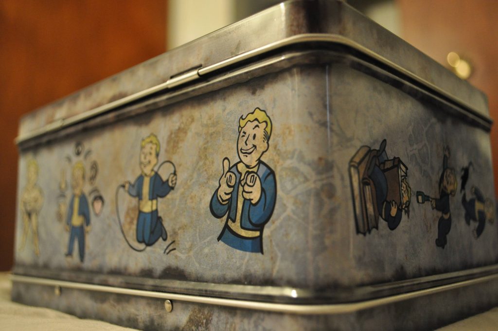 Close-up of rusted Fallout 4 tin box with Vault Boy in blue yellow suit finger-pointing pose Wallpaper
