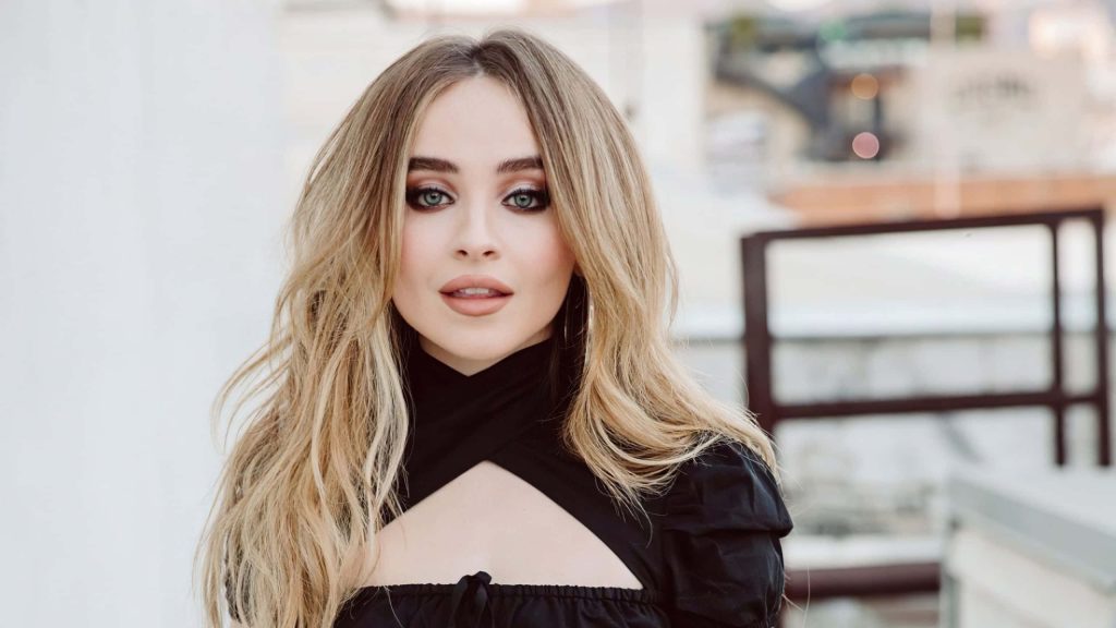 High-resolution portrait of Sabrina Carpenter with wavy blonde hair in chic black top Wallpaper