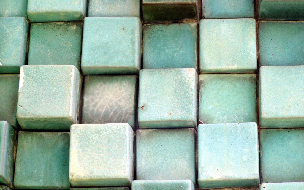 Macro photo of sage green ceramic blocks with crackled glaze and textured grid pattern wallpaper