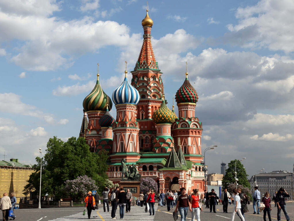 Tourists admire colorful domes of Saint Basils Cathedral Moscow bright sky iconic landmark background Wallpaper