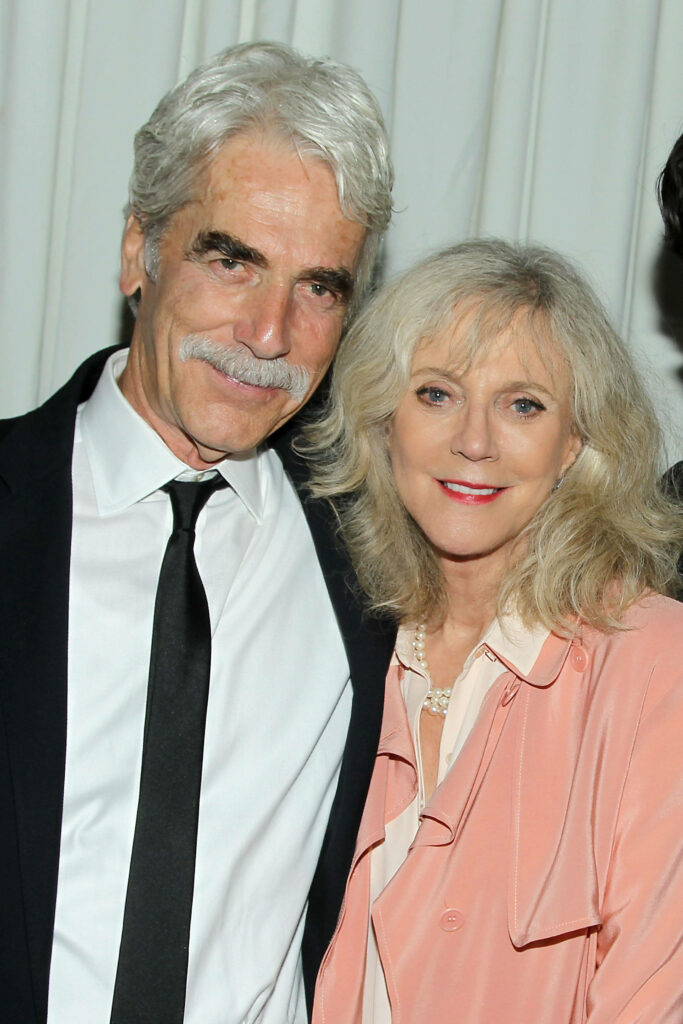 Sam Elliott and Blythe Danner smiling in formal attire against a light wallpaper background