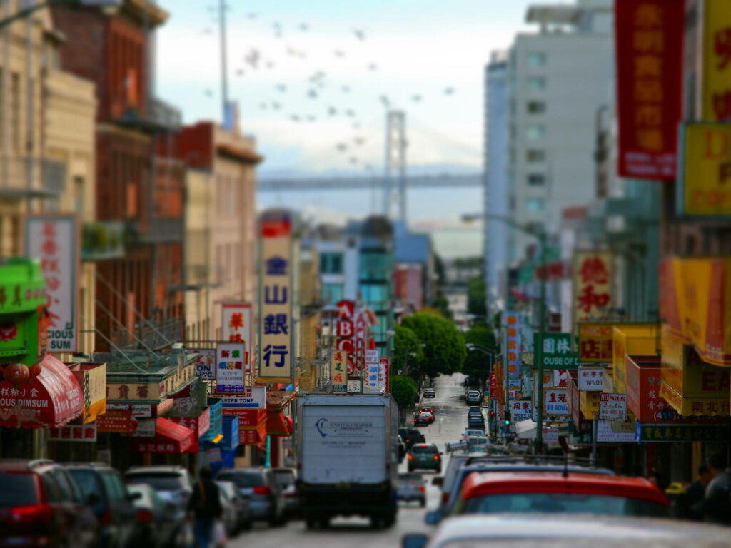 Vibrant San Francisco Chinatown street with colorful Chinese signs busy cars and iconic bridge background Wallpaper