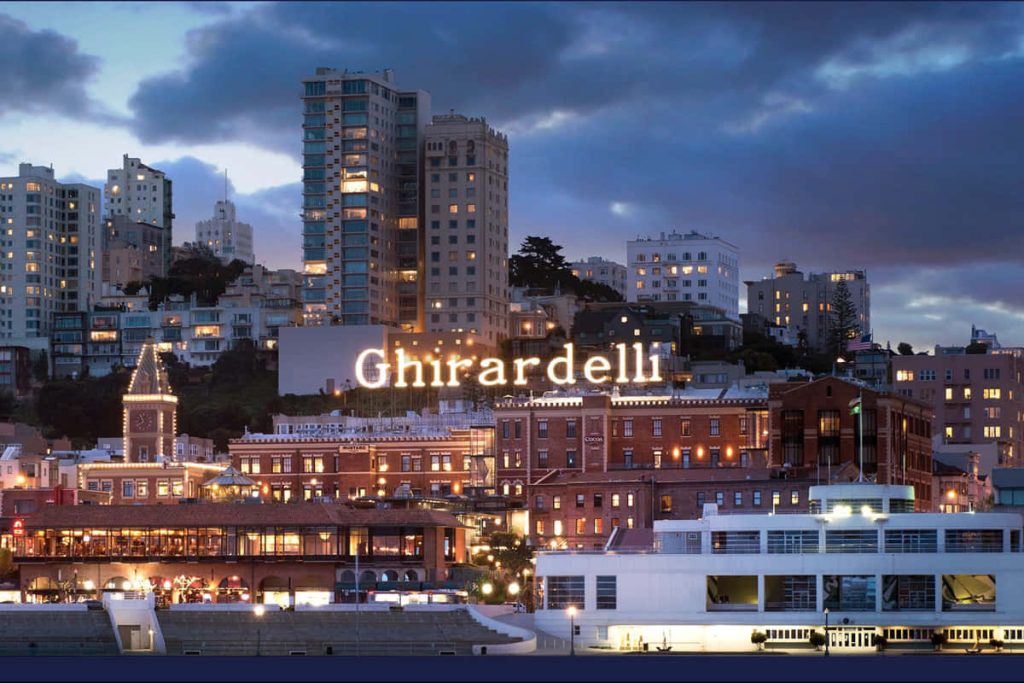 Ghirardelli Square glowing at twilight with San Francisco skyline and historic brick buildings Wallpaper