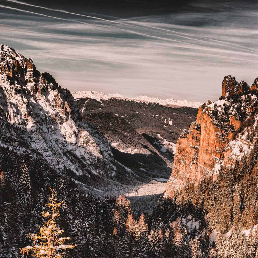 Dramatic San Vigilio mountains with orange cliffs snow-dusted pine forests and moody sky wallpaper